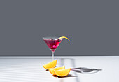 Composition of glass filled with red fruit cocktail near orange slides and zest placed on concrete table against grey background