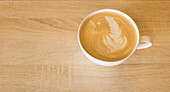 From above of white ceramic cup of aromatic hot cappuccino decorated with latte art placed on wooden table in cafe