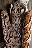 Top view of cut and whole sourdough baguettes with crunchy crust placed on wooden table