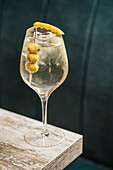 From above of crystal wineglass with Martini cocktail served with lemon zest and olives edge of wooden table