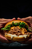 Crop anonymous person with appetizing burger with fresh lettuce pork and cheese on dark background