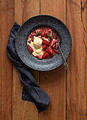 Draufsicht auf leckere flambierte Erdbeerhälften mit Vanilleeis in einem Teller auf einem Holztisch