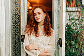 Charming young female with long ginger hair with her arms crossed in indoor garden with houseplants