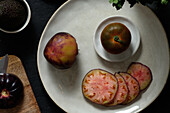 Draufsicht auf frische ganze und in Scheiben geschnittene schwarze Tomaten auf dem Tisch mit Avocado und grüner Minze bei der Zubereitung einer gesunden Mahlzeit