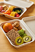 Von oben von Lunch-Boxen mit gesunden Lebensmitteln einschließlich Cracker Karotten-Sticks Trauben Kirschtomaten mit Kiwi Brokkoli Walnuss und Mandarine auf rosa Hintergrund
