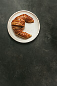 Top view composition with appetizing freshly baked crusty croissant served on white and black plate on table