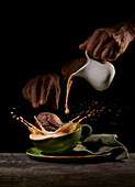 Crop anonymous person throwing tasty sweet cookies into green ceramic cup with splashing coffee on table in kitchen on black background