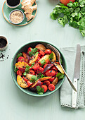 Top view of a raw tomato salad with fruit on a table with green tablecloth surrounded by healthy ingredients