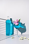 Glasflasche mit blauer Flüssigkeit in der Nähe eines Glases mit einem erfrischenden Cocktail mit Eis und Blumen auf einem Tisch vor weißem Hintergrund