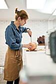 Young female with sharp knife cutting raw squash on chopping board while cooking in kitchen at home