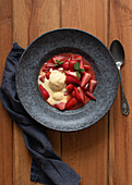 Top view of tasty flambeed strawberry halves with vanilla ice cream in plate on wooden table