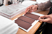 Anonymous person placing handmade chocolate bar on piece of paper while working in confectionery