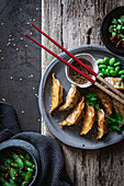 Gyozas with green beans and soy sauce with sesame seeds placed with chopsticks near bowls with spices and pea pods