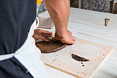 From above of crop anonymous male artisan rolling clay piece while creating plate in workshop