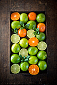 From above of ripe green limes and oranges placed in box on wooden rustic table