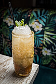 From above of tiki cup with cold alcohol drink with straw served with ice and decorated with fresh herb placed on blurred background