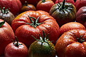 From above of appetizing fresh ripe tomatoes with drops of water with green leaves