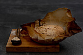 Komposition mit frisch gebackenem, rustikalem, rundem Sauerteigbrot auf Pergamentpapier auf einem Holzbrett mit Löffel und Weizenmehl