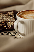 From above of cup of hot aromatic coffee with foam placed on wooden table and chocolate bar