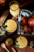 Glasses of delicious refreshing drinks with pear juice and fresh elderflower leaves on table with cinnamon sticks