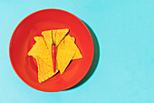Top view of hot chili pepper placed on crispy tortilla chips in red bowl on blue background