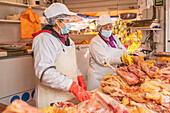 Peruanische Verkäuferinnen mit Gesichtsmasken und Schürzen stehen hinter der Theke mit rohem Hühnerfleisch während der Arbeit auf einem Wandermarkt