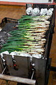 Haufen traditioneller katalanischer frischer grüner Kalzotten auf schwarzem Metallgrill mit Folie und glühender Holzkohle auf der Terrasse
