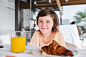 Delightful preschool kid looking at camera while sitting at table with food in cafeteria