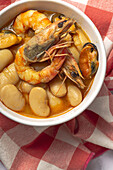 Close up of bowl with typical stew of beans with prawns, shrimps and mussels on a red checkered on a stone table