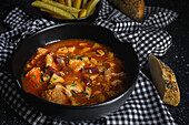 From above of tasty callos a la madrilena in black bowl near French fries and bread with seeds