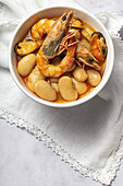 From above bowl with typical stew of beans with prawns, shrimps and mussels on a lace tablecloth and on a stone table