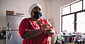 Venezuelan female in cloth face mask preparing arepas while looking forward at table with bowl at home