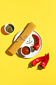 From above appetizing fresh dry spaghetti with red sauce and spice dip red peppers on yellow background