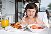 Delightful preschool kid looking at camera while sitting at table with food in cafeteria