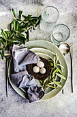 Cutlery set for Easter dinner with olive tree branches and eggs on a bird nest on a concrete background