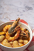 From above bowl with typical stew of beans with prawns, shrimps and mussels on a red checkered on a stone table