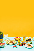 Geschirr mit Nachos und Hühnersalat neben einer Flasche Bier und einem Glas Limonade vor gelbem Hintergrund