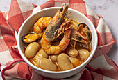From above bowl with typical stew of beans with prawns, shrimps and mussels on a red checkered on a stone table