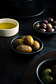 From above tasty juicy green brown yellow olives and oil in black and white bowls on black table
