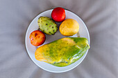 Draufsicht auf köstliche reife ganze exotische Papaya und Kaktusfrucht mit Mango und Pflaumen auf weißem Keramikteller serviert und auf Bett gelegt