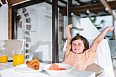 Delightful preschool kid stretching with closed eyes while sitting at table with food in cafeteria