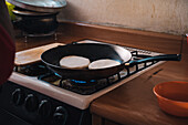 Pfanne mit venezolanischen Arepas, die auf einem Gasherd in einer Küche zu Hause gebraten werden