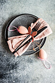 Von oben gedeckter Tisch für das Osteressen mit rosa Serviette und Eiern auf Betonhintergrund