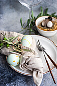 From above cutlery set for Easter dinner with olive tree branches and eggs on a bird nest on a concrete background