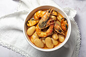 From above bowl with typical stew of beans with prawns, shrimps and mussels on a lace tablecloth and on a stone table