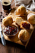 From above delicious homemade muffins and raspberry jam on wooden board near coffee on table