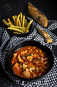 From above of tasty callos a la madrilena in black bowl near French fries and bread with seeds