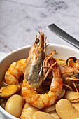 Close up of bowl with typical stew of beans with prawns, shrimps and mussels on a lace tablecloth close to a spoon and on a stone table