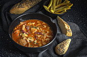 From above of tasty callos a la madrilena in black bowl near French fries and bread with seeds