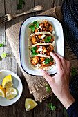 Von oben Hand mit Blumenkohl-Snack-Tacos in Schale und Zitronenstücken in Teller auf Holztisch